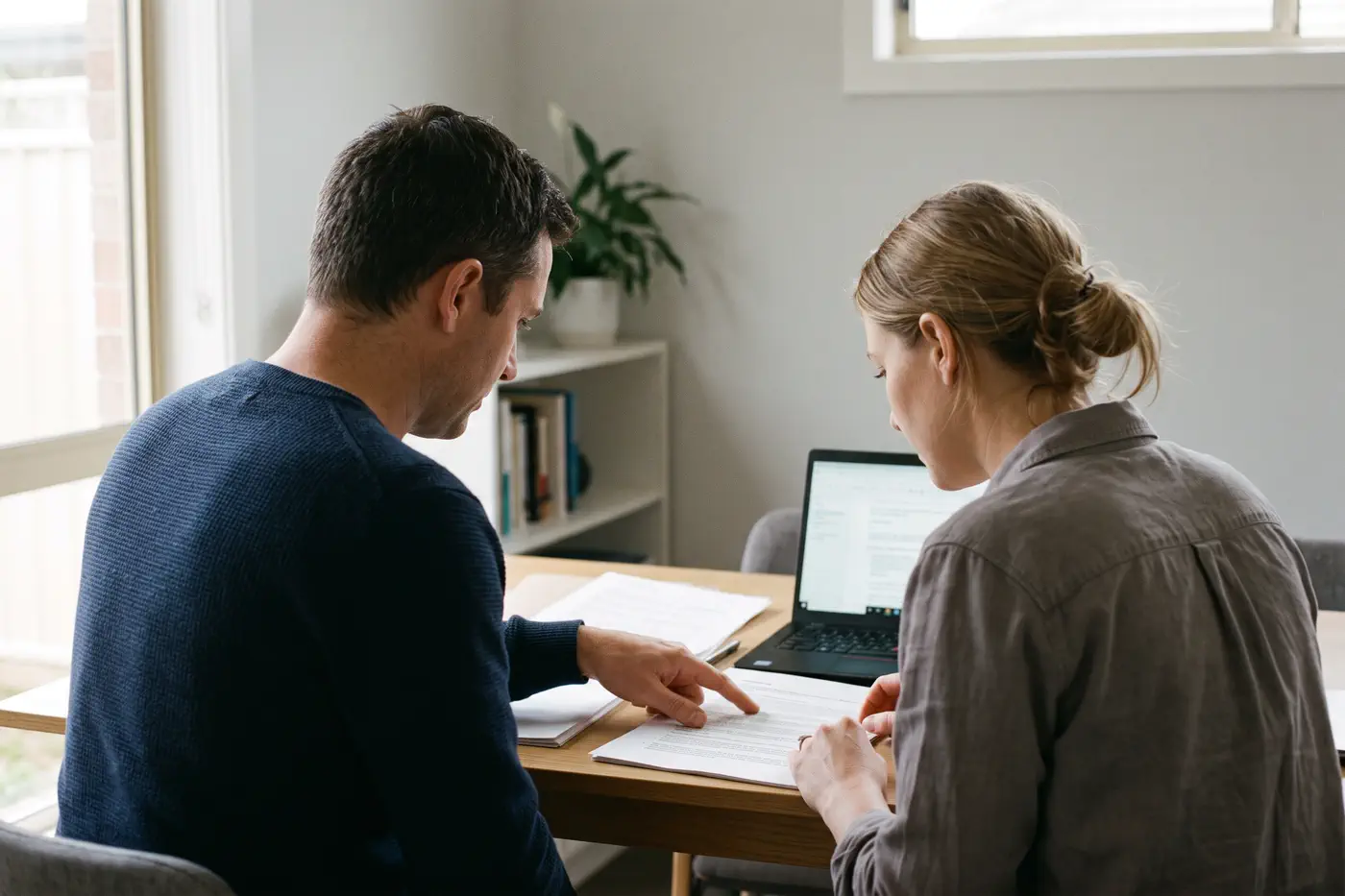 Two people reviewing printed claim documents and a laptop